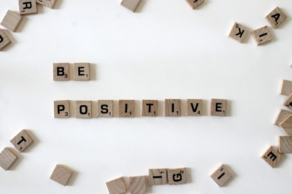 Scrabble letters arranged to spell "be positive" on a wooden board