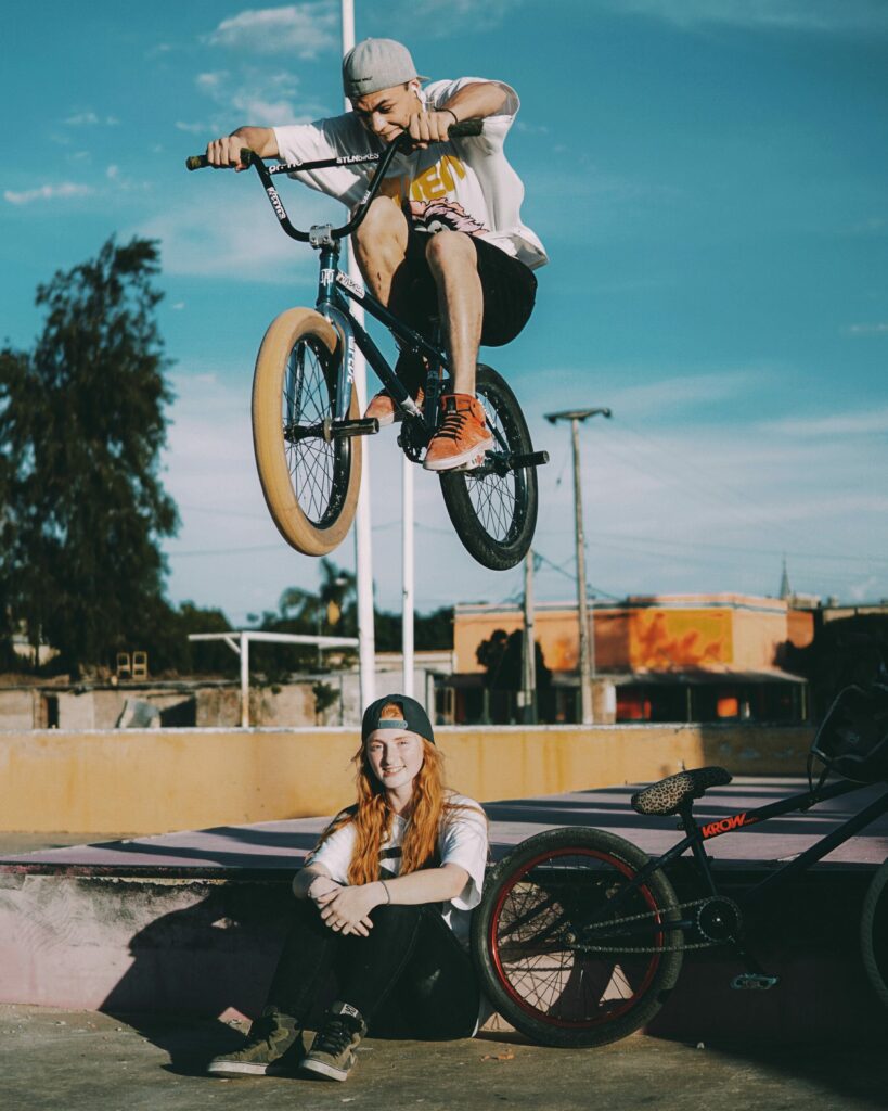 A man on a bike jumping a girl that is sitting