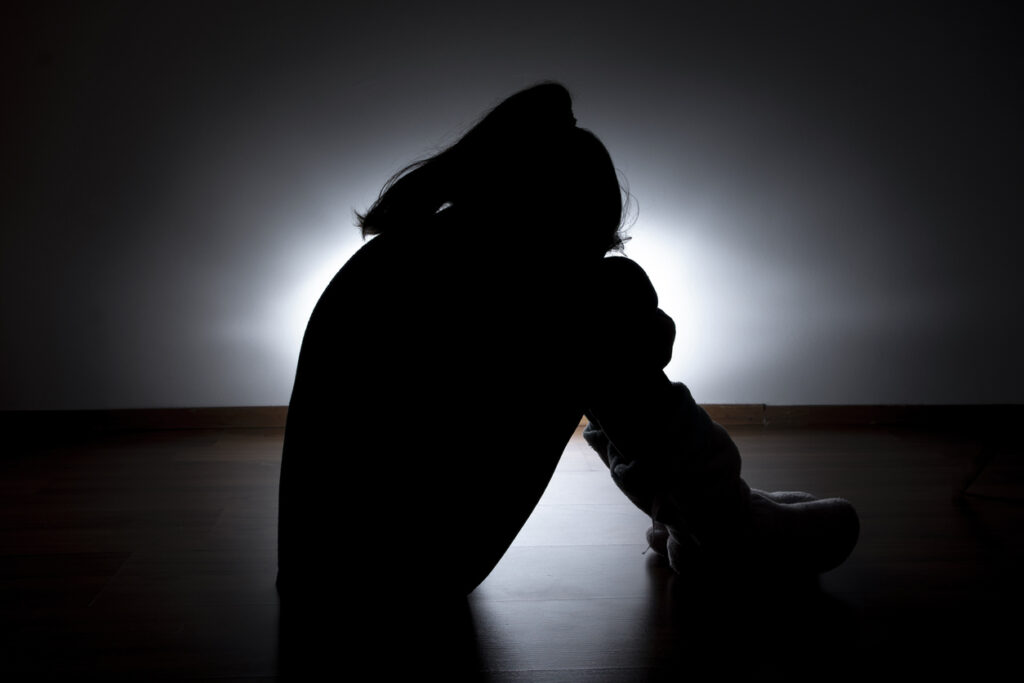 A dark room features the silhouette of a woman sitting on the floor