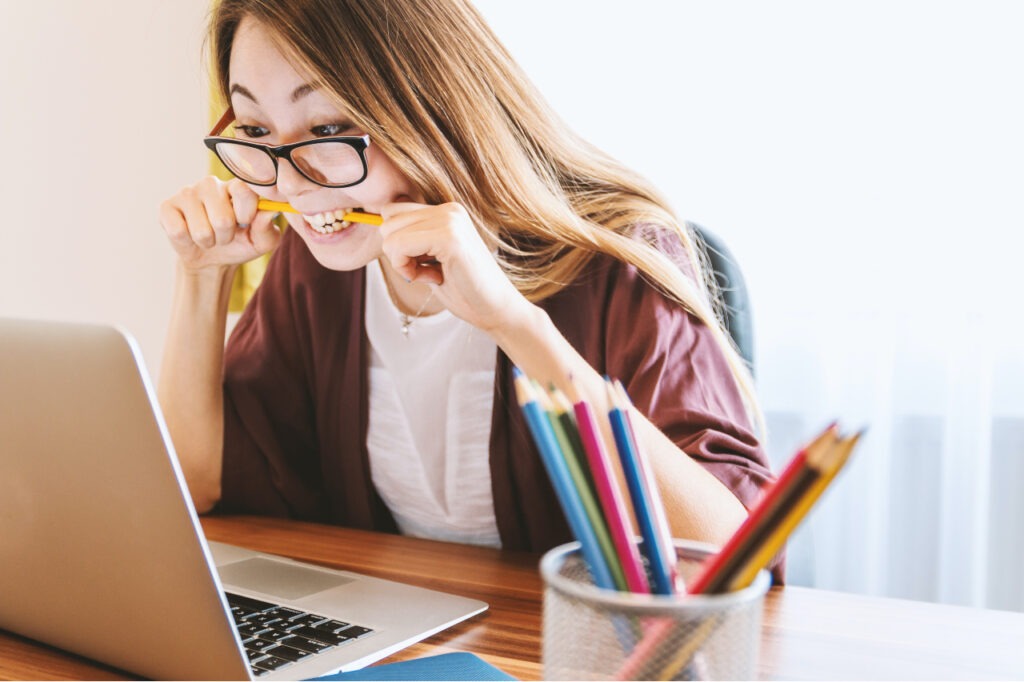 A woman biting a pencil in front of her laptop