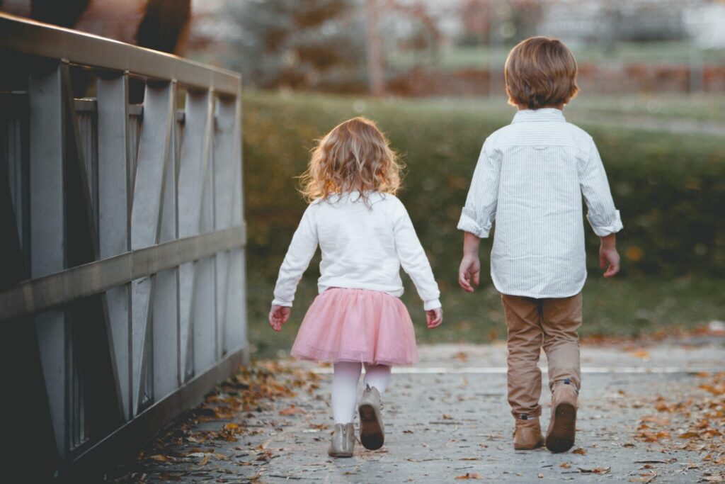 Two young children stroll down a leaf-covered path