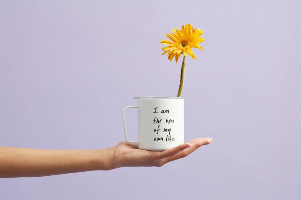 A hand gently holds a mug with a blooming flower
